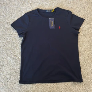 Mörkblå t-shirt från Polo Ralph Lauren - Klassisk mörkblå t-shirt från Polo Ralph Lauren med röd broderad logga på bröstet. T-shirten har rund halsringning och korta ärmar. Tillverkad i mjuk bomull för en skön och stilren look.