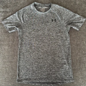 Grå tech t-shirt från Under Armour XS - Säljer en gråmelerad tech t-shirt från Under Armour i storlek XS. T-shirten är kortärmad, har rund hals och är tillverkad i 100% polyester för en lätt och luftig känsla. Perfekt för träning med loose fit och diskret logga på bröstet.