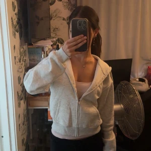 Ljusgrå hoodie med dragkedja från Gina Young - Ljusgrå hoodie med dragkedja och huva. Tröjan har snörning i huvan, ribbade muddar och fickor framtill. Perfekt för chill dagar och enkel att matcha med det mesta. Klassisk och basic stil som funkar året runt. De har mjukt material inuti och fungerar som en vanlig varm hoodie. Den är lite för liten på mig för min smak så den har använts en enstaka gång men inget har slitits eller något på den.