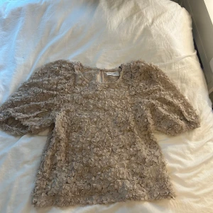 Beige blommig blus - Aldrig använd. Supersöt beige blus från Holly & Whyte med 3D-blommor över hela tyget. Puffiga korta ärmar och rund halsringning. Blusen är i spets🥰Passar även S och M😗