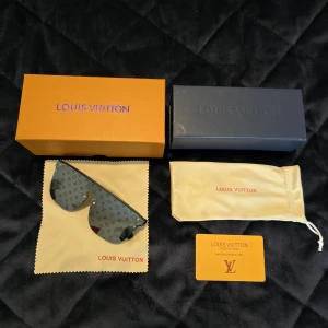 Svarta Louis Vuitton solglasögon - Exklusiva svarta solglasögon från Louis Vuitton med monogrammönster på glasen och breda svarta bågar. Snygg futuristisk sköldform och diskret logga på skalmarna. Kommer med originalbox, putsduk, fodral och äkthetskort.