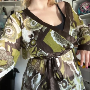 Grön babydoll topp  - Tunnt, fint material med blommor och andra saker, samt ett brunt band runt. Säljer för jag använder den inte längre 
