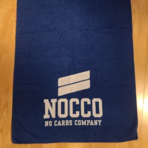 Blå NOCCO Handduk med vit text - LIMITED EDITION Handduk från NOCCO med vit text och logga. NYSKICK. Enbart använd vid reklatillfälle