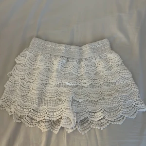 Vita spets-shorts från Chelsea - Superfina vita shorts från Chelsea med bred resår i midjan och flera lager volangig spets. De har en romantisk och bohemisk vibe, perfekta för varma dagar. Luftiga och bekväma med snyggt mönstrad spets som ger en extra detalj till outfiten. Storlek xs/s💞