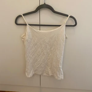Vit enkel linnetopp med smala band - Säljer en vit linnetopp med smala axelband och rak passform. Toppen är ärmlös och har en klassisk, stilren look som funkar till allt. Perfekt för varma dagar eller som lager under skjorta eller tröja.