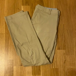 Beige chinos från Polo Ralph Lauren - Snygga beige chinos från Polo Ralph Lauren i klassisk rak modell. Byxorna har bälteshällor och är tillverkade i mjuk bomull, perfekta för en clean och stilren look. Passar dig som gillar tidlös stil och vill ha ett par riktigt schyssta byxor.
