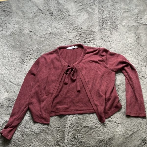 Vinröd kofta med knyt från 157 - Söt vinröd kofta från 157 i stickat material. Modellen är croppad med långa ärmar och har en snygg knytning framtill. Perfekt att slänga över en topp för en chill och trendig look.