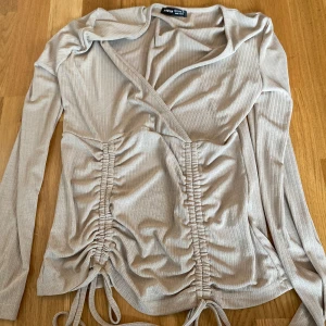 Beige omlottopp med snörning från SHEIN - Trendig beige omlottopp från SHEIN med långa ärmar och ribbat tyg. Toppen har snygg snörning framtill och v-ringad hals. Perfekt för dig som gillar en stilren men ändå cool look.
