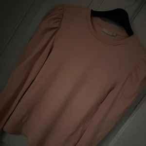 Ljusrosa långärmad topp från Pieces - Supersöt ljusrosa långärmad topp från Pieces med puffade axlar och rund halsringning. Tillverkad i mjuk bomull som känns skön mot huden. Perfekt för dig som gillar en enkel men ändå trendig look.