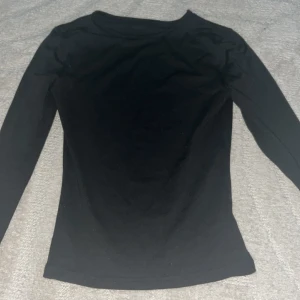 Svart långärmad bomullströja - Enkel och stilren svart långärmad tröja i mjuk bomull. Perfekt basplagg med rund hals och smal passform som funkar till allt. Snygg att bära som den är eller under en jacka.