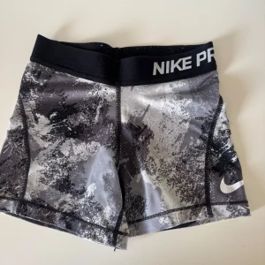 Nike Pro Dri-FIT träningstights shorts barn - Nike Pro Dri-FIT shorts i tight modell med svart och grått camouflage-liknande mönster. Bred svart resår med Nike Pro-tryck i vitt. Tillverkade i stretchigt syntetmaterial som andas, perfekta för träning och sport.