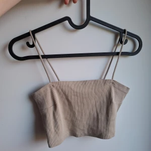 Beige ribbad tubtopp från Gina Tricot - Säljer en beige ribbad tubtopp från Gina Tricot i storlek M. Toppen har smala axelband och är croppad, perfekt till sommaren. Materialet är mjukt och stretchigt, vilket gör den superbekväm och enkel att styla med jeans eller kjol.