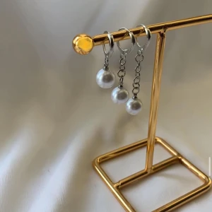 Silvriga örhängen med pärlor - Säljer ett par trendiga silvriga örhängen med hängande kedjor och vita pärlor. Örhängena har minimalistisk design med runda hoops och kedjor som avslutas med glansiga pärlor. Perfekta för dig som gillar stilrena smycken med en elegant touch.