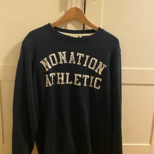 Mörkblå sweatshirt från Nonation - Mörkblå sweatshirt från Nonation Athletic i storlek XXL. Tröjan har ett stort vitt tryck med texten 'NONATION ATHLETIC' på bröstet och klassisk rund hals. Perfekt för en avslappnad och sportig stil.