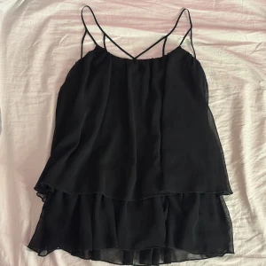 Svart volang linne - Snyggt svart volang linne från Gina Tricot som passar perfekt till fina tillfällen eller fest, men även till vardags. Den har två lager volanger och smala axelband. Använd 1 gång💕 skriv för fler bilder eller mått och pris kan alltid diskuteras!