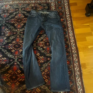 Mörkblå Lee jeans med raka ben - Säljer ett par klassiska mörkblå jeans från Lee med snyggt slitna detaljer och raka ben (straight leg). Jeansen har fem fickor, Lee-läderpatch bak och kontrastsömmar. Perfekta för dig som gillar en tidlös och avslappnad look.