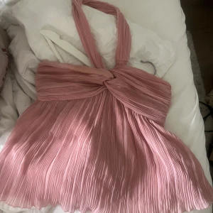 Plisserad rosa halterneck topp - Supersöt plisserad topp i ljusrosa med halterneck och twistad detalj framtill. Luftig och flowy modell som ger en romantisk vibe. Perfekt för varma dagar när du vill sticka ut lite extra.