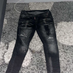 Svarta skinny jeans med slitningar - Säljer ett par svarta skinny jeans med coola slitningar och färgstänk. Jeansen har en tight passform och klassisk femficksdesign. Perfekta för dig som gillar en edgy streetstil.