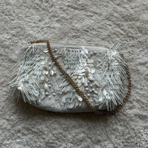 Vit pärlbroderad väska med kedja - Superfin vit kuvertväska från H&M med massor av pärl- och paljettbroderier, 3D-blommor och en snygg guldfärgad kedja. Väskan har dragkedja upptill och är fodrad inuti. Perfekt för att lyfta vilken outfit som helst. Nypris 699kr 