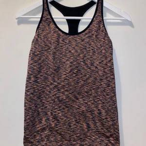 Mönstrad träningstopp från Gina Tricot - Supersnygg träningstopp från Gina Tricot i svart och orange mönster. Modellen är ärmlös med brottarrygg och har en tight passform som sitter perfekt under träningspasset. Materialet är mjukt och stretchigt syntet, perfekt för gymmet eller löprundan.