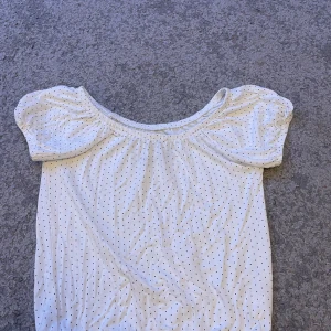 Vit prickig t shirt med puffärm - Supersöt vit blus med små svarta prickar och puffiga korta ärmar. Den har en bred, elastisk urringning som kan bäras offshoulder. 