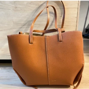 Brun väska  - Stilren och rymlig shoppingväska  i brunt skinn med minimalistisk design. Väskan har två handtag, magnetknäppning och en matchande innerficka med dragkedja. Perfekt för dig som vill ha plats för allt du behöver under dagen.