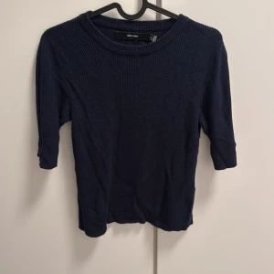 Mörkblå stickad tröja Vero Moda - En stilren mörkblå stickad tröja från Vero Moda med ribbad struktur. Tröjan har rund halsringning och trekvartsärm, vilket gör den enkel att matcha med både jeans och kjol. Perfekt för dig som gillar en clean och klassisk look.