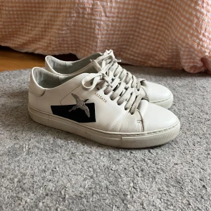 Axel Arigato Sneakers - Så snygga vita Axel Arigato sneakers! En grå fågel och även lite svart på sidan. Bra skick men lite smutsiga skosnören som enkelt går att tvätta. Storlek 39. Säljer direkt för 450kr!