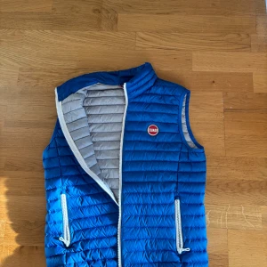 Blå dunväst från Colmar - Snygg blå dunväst från Colmar med quiltad design och grå insida. Västen har två dragkedjeförsedda fickor och vit dragkedja framtill. Perfekt för lager-på-lager och har en grischig vibe med Colmar-logga på bröstet. Passar folk som är 153-160 !!!100% riktig!!! Original pris 1300kr mitt pris endast 899kr!!!