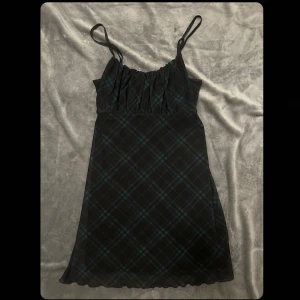 Grunge klänning från Hollister  - Supersöt kort klänning från Hollister i svart med grönt rutmönster. Justerbara smala axelband. Perfekt för dig som gillar en klassisk grunge stil.