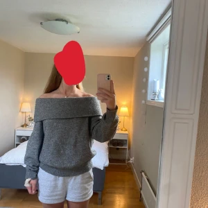 Grå offshoulder stickad tröja H&M - Mysig grå stickad tröja från H&M med bred offshoulder-krage. Tröjan har lång ärm, ribbade muddar och en loose fit som ger en chill vibe. Perfekt för lager-på-lager under höst och vinter. Har ett litet hål på höger arm men inget märkbart. Storlek S