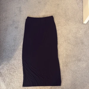 Svart långkjol i mjukt tyg - Enkel och stilren svart långkjol med rak passform. Kjolen är gjord i ett mjukt och följsamt material som ger en snygg siluett. Perfekt att matcha med en crop top eller oversized tröja för en chill look.