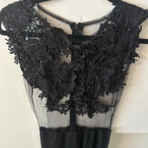 Svart jumpsuit - Supersnygg svart jumpsuit  med transparent mesh upptill och stora blommiga spetsapplikationer över byst och axlar. Jumpsuit  har rund halsringning och dragkedja bak. Perfekt för dig som vill sticka ut med en elegant och unik look. Du kan hitta mer på min sida.