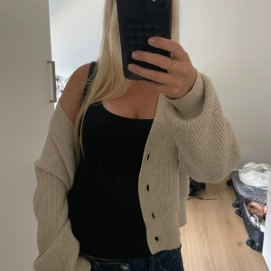 Beige ribbad kofta med knappar - Säljer en beige ribbstickad kofta med stora knappar framtill. Koftan har en loose passform och långa ärmar, perfekt att slänga över ett linne eller t-shirt. Enkel och stilren design som funkar till många outfits.