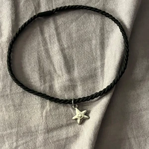 Svart Choker Med Stjärna - Chokerhalsband med tvinnad svart snodd och ett silverfärgat hänge i form av en glad stjärna. 🌻