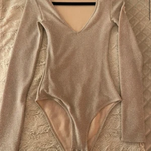 Glittrig beige långärmad body - Glittrig beige body med v-ringning och lång ärm. 