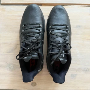 Svarta golfskor från Under Armour - HERR  Golfskor i storlek 44 från Under Armour. Använd endast ett fåtal gånger för det var felköp av storlek. Skorna är i bra skick men använda på golfbanan under alla väder därav lite smutsiga även fast de är sparsamt använda. Under skon saknas en av peggarna (se bild) vänster bak.