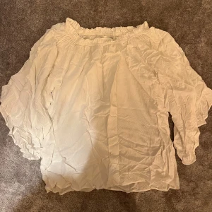 Vit offshoulder blus med volang - Säljer en luftig vit blus med offshoulder-modell och volangdetaljer längs halsringningen. Blusen har trekvartsärmar och är gjord i ett tunt, skönt bomullstyg. Perfekt för dig som gillar romantisk och avslappnad stil.