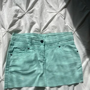 Jeanskjol - Mintgrön jeanskjol som är klippt, har en liten fläck på framsidan men inget som man märker av. MIDJEMÅTT: 38 cm, LÄNGD: 31.5 cm