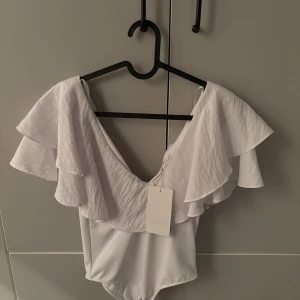 Vit volangbody från Zara - Superfin vit body från Zara med breda volangärmar och djup v-ringning. Materialet känns mjukt och följsamt. Helt ny med prislapp. Köp innan fredag och jag postar tills dess