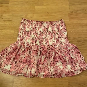 Rosa blommig volangkjol - Supersöt kort kjol med rosa och vita blommor och volanger. Kjolen har smock upptill som ger en tight passform och volangig nederdel som ger extra flow. Perfekt för dig som gillar romantisk och feminin stil. Plagget kan användas både som kjol och topp som ni ser att jag gör på bild nmr 2. Väldigt smidigt, används 2 gånger ungefär så väldigt ny skick! Pris kan diskuteras vid snabb affär!🥰