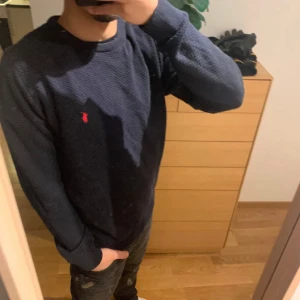 Mörkblå stickad tröja från Polo Ralph Lauren - Snygg mörkblå stickad tröja från Polo Ralph Lauren med klassisk rund halsringning och röd broderad logga på bröstet. NYPRIS:2299Kr MITT PRIS: 329Kr