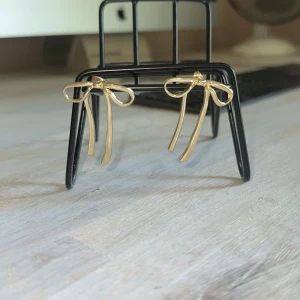 Guldiga örhängen med rosettform - Snygga örhängen i guldmetall formade som rosetter med långa band. De har en stilren och lekfull design som verkligen sticker ut. Perfekta för dig som vill ha något unikt och trendigt i smyckeslådan.