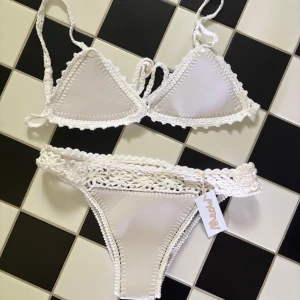 Vit virkad bikini från Meow - Superfin vit bikini från Meow med virkade detaljer och knyt i sidorna. Triangelformad överdel och trosor med bred virkad kant ger en boho-vibe. Perfekt för stranden eller poolen, och riktigt snygg till solbrännan! Underdelen är i storlek S och överdelen i storlek M men skulle säga att den passar XS-S💕