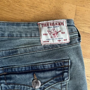 True Religion Joey Low Rise Flare Jeans - Snygga ljusblå jeans från True Religion, modell Joey med låg midja och utsvängda ben. Klassiska detaljer med synliga sömmar, fickor med lock och logoknappar. Helt ny oanvänd.