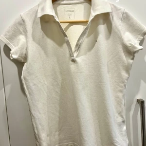 Vit pikétröja från Boomerang, stl L - Klassisk vit pikétröja från Boomerang i storlek L. Tröjan har korta ärmar, krage och en liten broderad logga på bröstet. Tillverkad i mjuk bomull med lite stretch för extra komfort. Perfekt för en clean och stilren look.