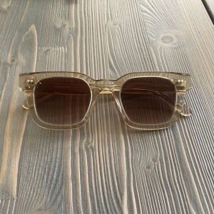 Chimi Solglasögon | Ecru 04 - Snygga solglasögon från Chimi i modellen Ecru 04 med transparent beige båge och bruna tonade glas. Ramen är fyrkantig och tillverkad i ett lätt syntetmaterial. Perfekta för dig som vill ha en clean och modern look med en touch av retro.