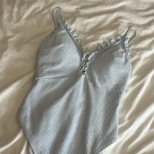 Randig baddräkt från H&M i blåvitt - Supersöt baddräkt från H&M med smala blå och vita ränder, volangkant vid bysten och smala axelband. V-ringad framtill med snygg knyt-detalj. Perfekt för stranden eller poolen i sommar! Helt oanvänd och köpt för 299kr. storlek M men skulle säga att den passar S mer☺️