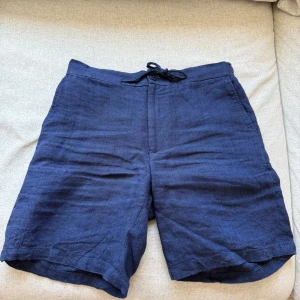 Marinblå linneshorts från These Glory Days - Snygga marinblå shorts i 100% linne från These Glory Days. Normal passform, snörning i midjan och bakfickor med knappar.