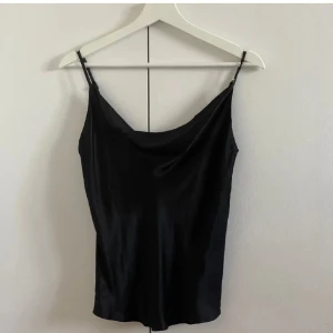 Svart topp - Svart topp i storlek xs från Kappahl. Tunna reglerbara axelband, liten slits nere vid sidorna (bild 4), drapering vid hals linningen. Materialet syns bäst på bild 4. Är helt oanvänd med lappen kvar. Hittar den inte på hemsidan så osäker om den fortfarande säljs. Köparen betalar frakten!